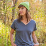 Žena v zelené čepici, zelených kalhotách a Merino tričku s výstřihem do V dámské - šedé (135 g) z wełny merino 100% venku.