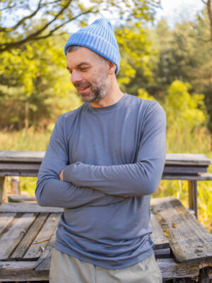Pánské merino tričko s dlouhým rukávem v šedé barvě na modelu v přírodě. Funkční merino oblečení z 100% merino vlny, ideální pro turistiku, cestování i každodenní nošení.