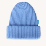 Světle modrá pletená čepice s ohrnutým okrajem a malou modrou visačkou na boku, zobrazená na hladkém smetanovém pozadí.