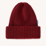 Žebrovaná pletená čepice s ohrnutou manžetou a malou modrou visačkou na boku, zobrazená na hladkém světlém pozadí.