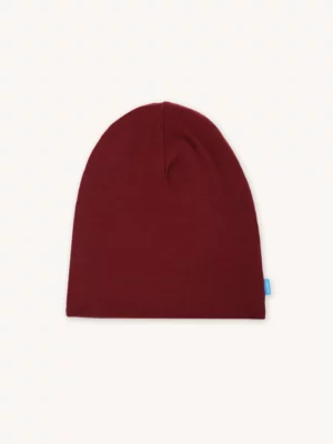 Na světlém pozadí je položena obyčejná bordó čepice s kšiltem. Kšiltovka má jednoduchý bezešvý design s malou modrou visačkou na boku.