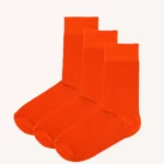 Tři páry zářivě oranžových ponožek jsou úhledně uspořádány v řadě na hladkém bílém pozadí.