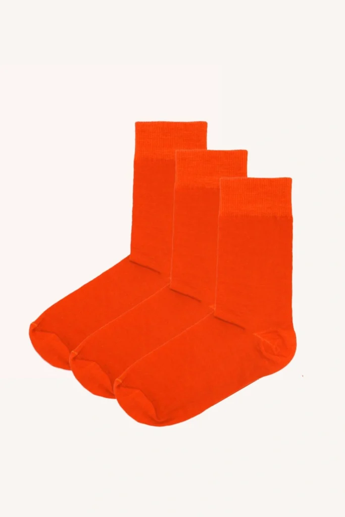 Tři páry zářivě oranžových ponožek jsou úhledně uspořádány v řadě na hladkém bílém pozadí.