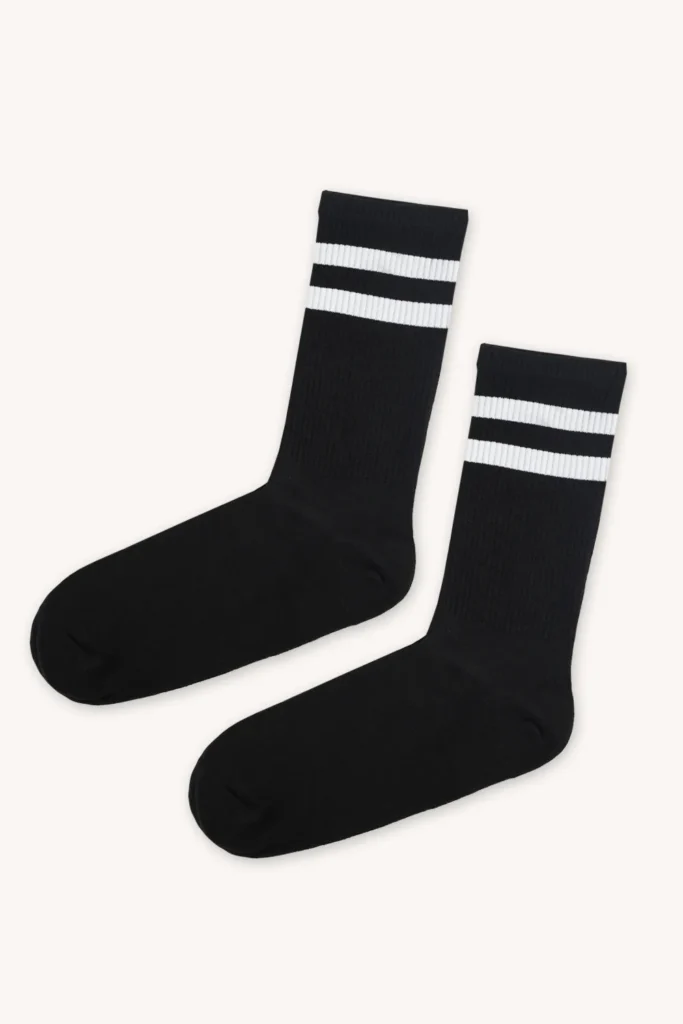 Pár černých ponožek s dvěma bílými vodorovnými pruhy u horního okraje, zobrazenými na hladkém světlém pozadí.