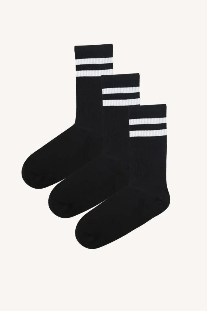 Tři páry černých ponožek se dvěma bílými pruhy u horního okraje, které jsou vedle sebe na hladkém světlém pozadí.