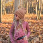 Dívka ve starorůžovém Merino termoprádle z wełny merino 100% s dlouhým rukávem (180 g), čepici a brýlích mezi podzimními listy.