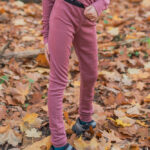 Dítě venku na podzimních listech má na sobě Merino termoprádlo legíny dětské - starorůžová (180 g) z wełny merino 100%.