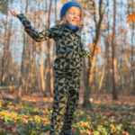 Dítě v Merino termoprádlo legíny dětské - olivové trojúhelníky (190 g) z wełny merino skáče radostí v podzimním lese.